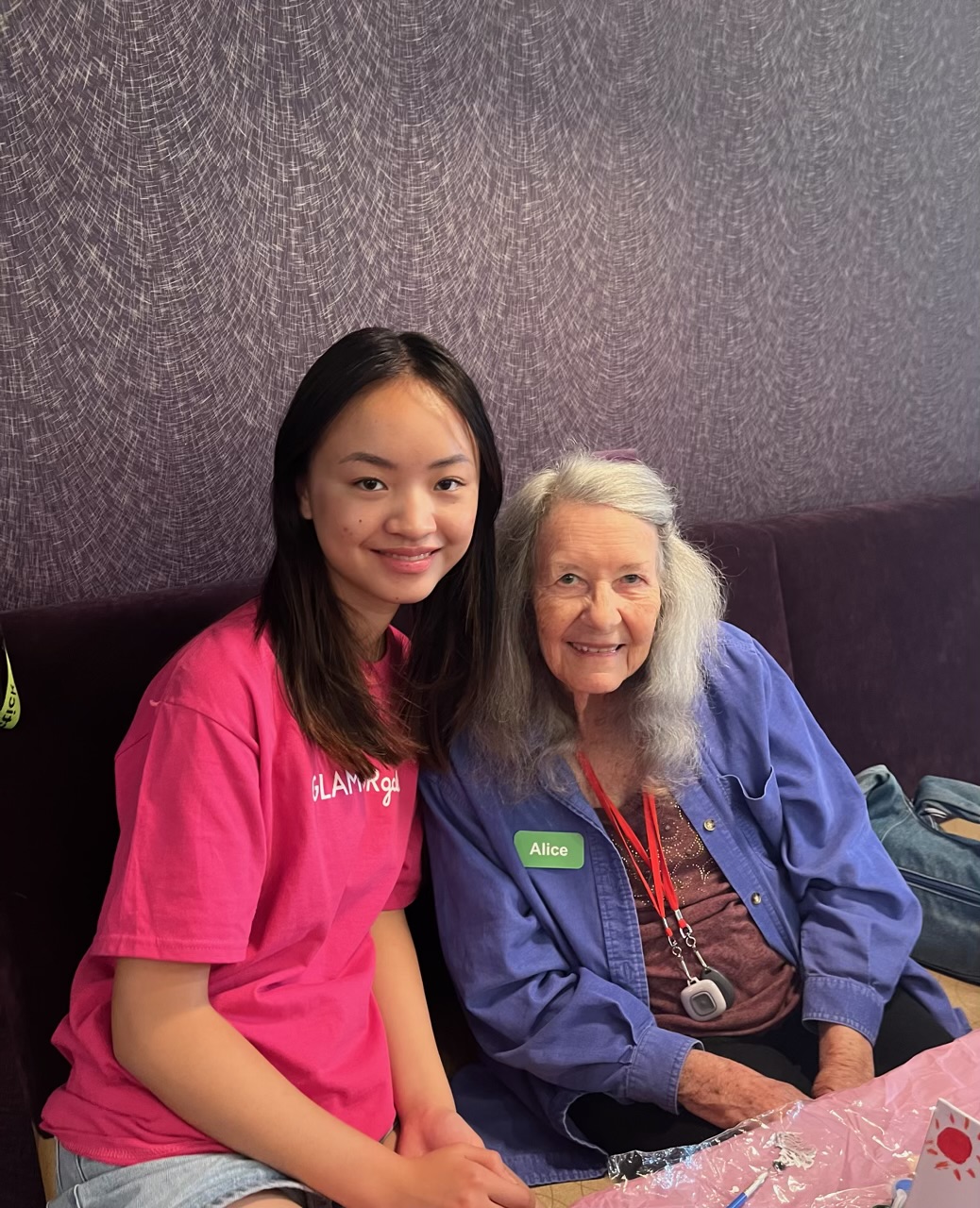 Staff taking a happy picture with senior resident Young girl smiling and sitting nest to an elderly resident during a crafting activity.