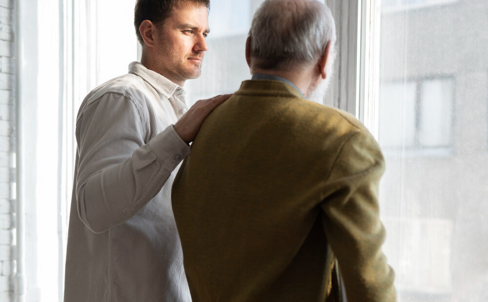 adult son talking to senior parent adult son comforting senior father while discussing senior living options
