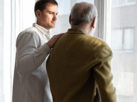 adult son comforting senior father while discussing senior living options