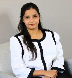Portrait of Tasleem Begum seated, wearing a white blazer with black trim.