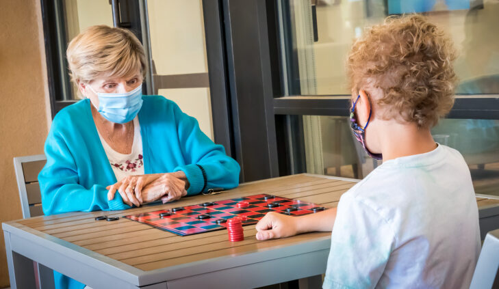 Senior resident playing checkers with a child during an intergenerational visit at Amaran Senior Living memory care in Albuquerque.