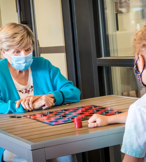 Senior resident playing checkers with a child during an intergenerational visit at Amaran Senior Living memory care in Albuquerque.